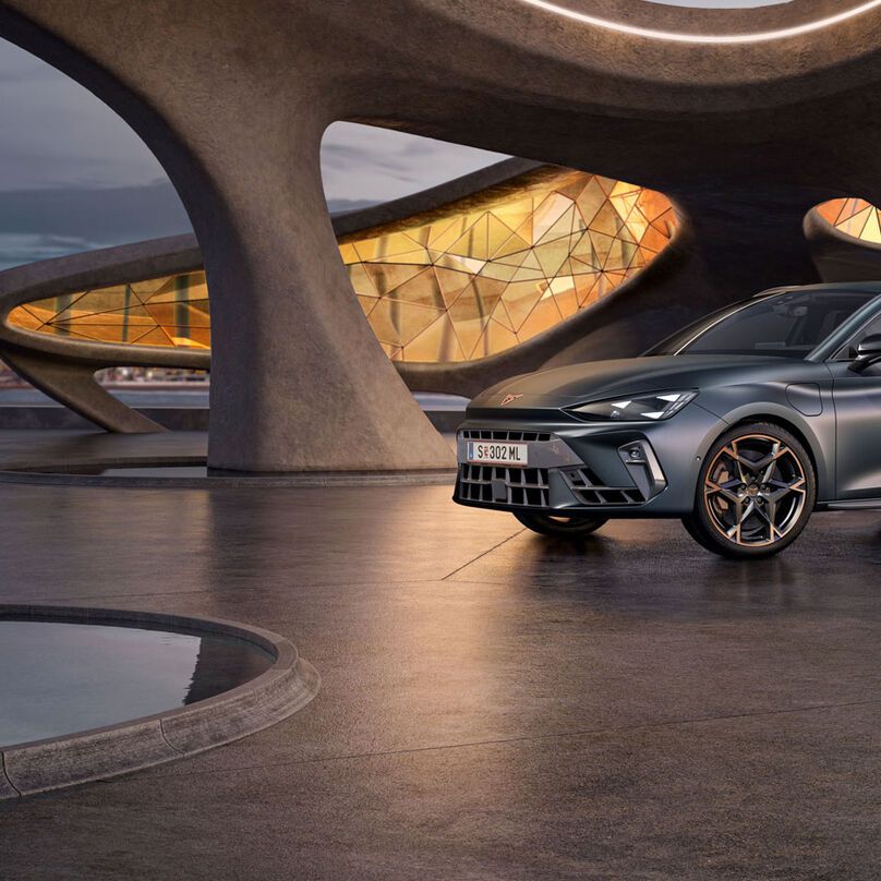 Schräge Vorderansicht eines grauen CUPRA Leon SP Kombi, der in einem modernen Parkhaus parkt.