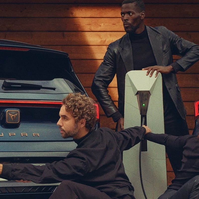 Zwei CUPRA Born links und rechts neben einer Ladesäule, eine Gruppe Tänzer posiert vor den Fahrzeugen.