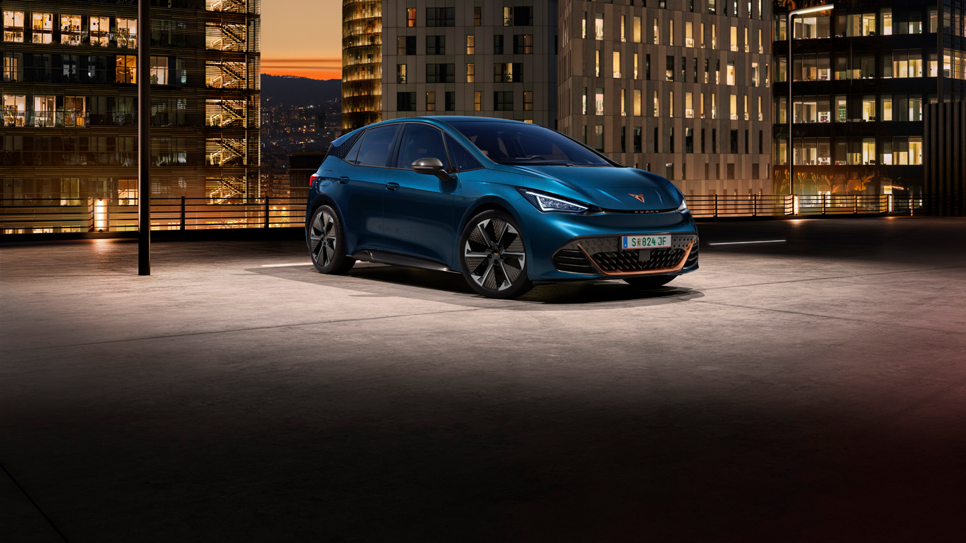 Ein blauer CUPRA Born auf dem Dach eines Parkhauses. Im Hintergrund beleuchtete Gebäude bei Nacht.