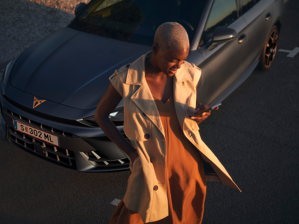 Frau sieht auf das Handy vor dem CUPRA Modell.