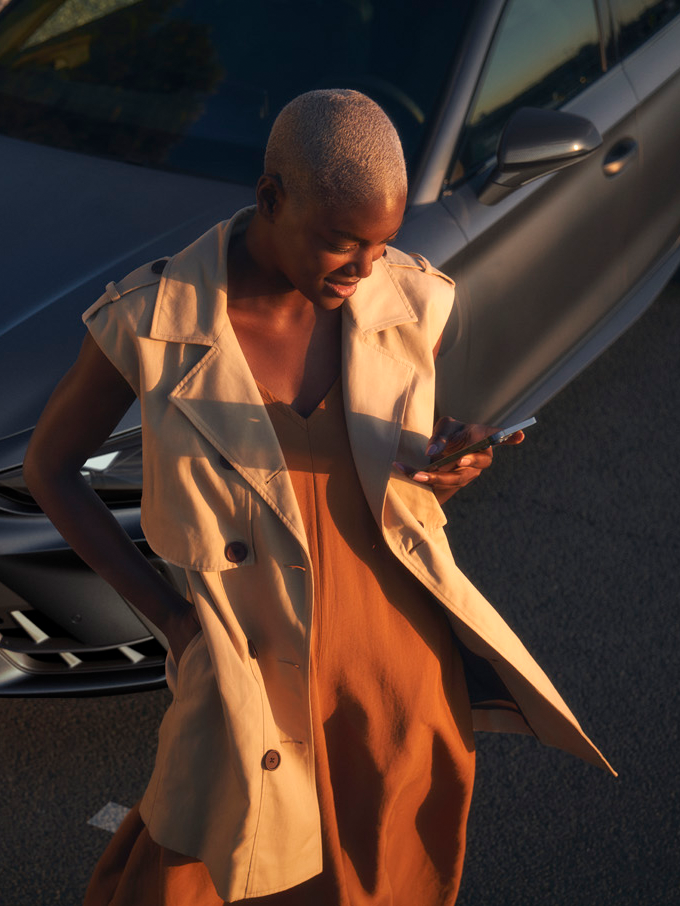 Frau sieht auf das Handy vor dem CUPRA Modell.