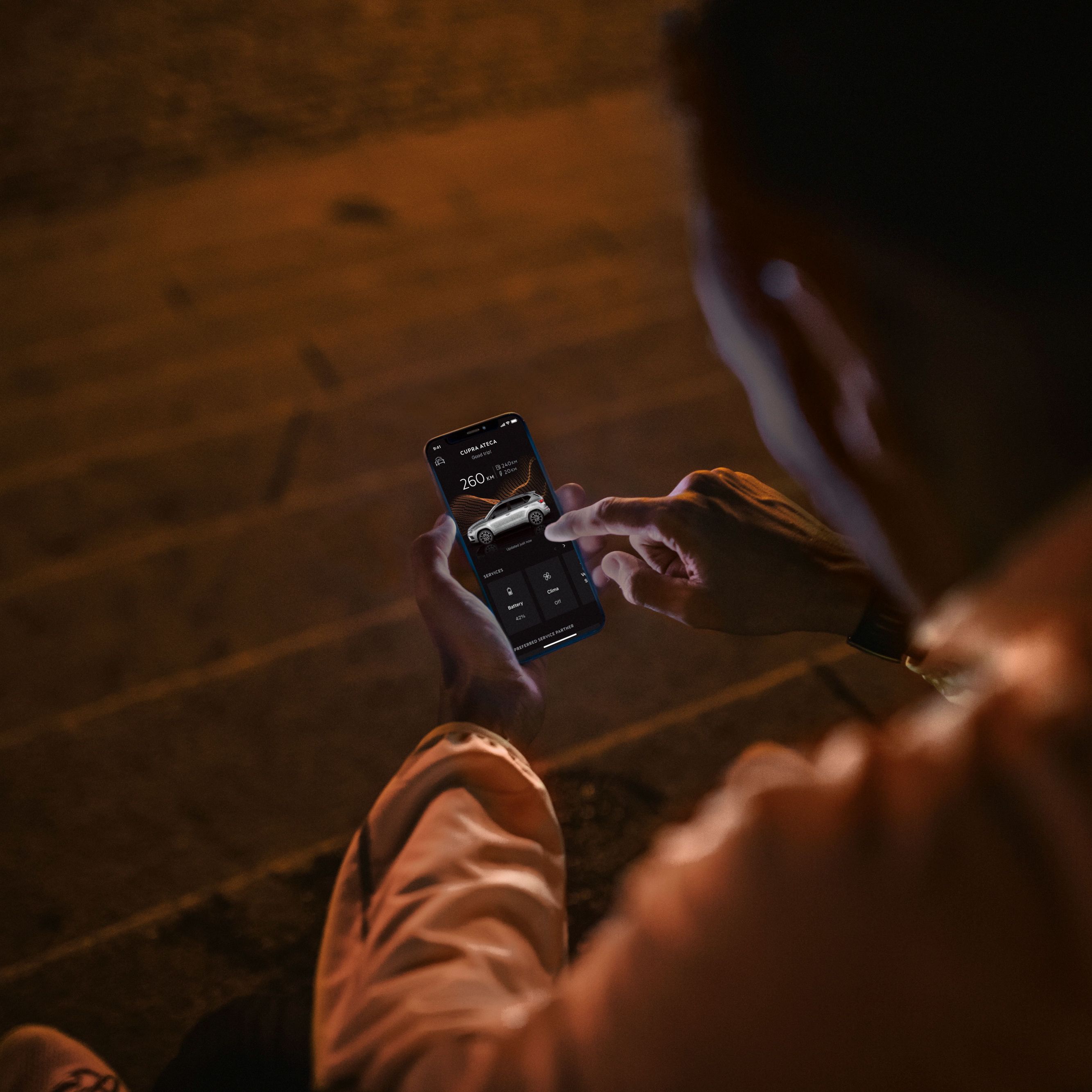 Eine Person sitzt nachts auf Treppenstufen und nutzt CUPRA Connect auf einem Smartphone.