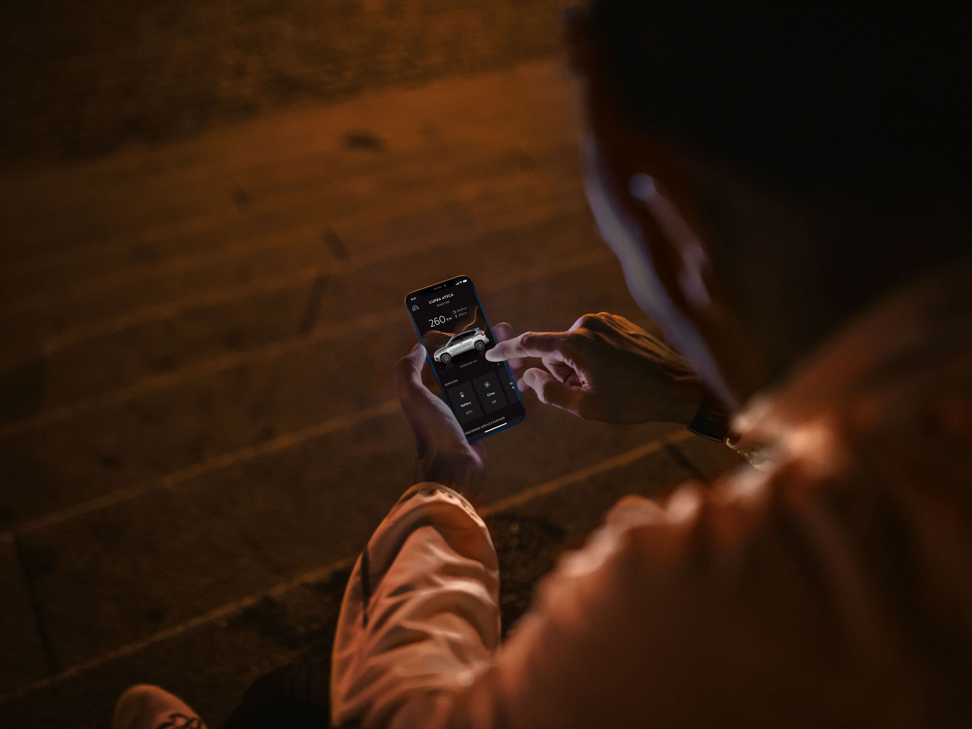 Eine Person sitzt nachts auf Treppenstufen und nutzt CUPRA Connect auf einem Smartphone.