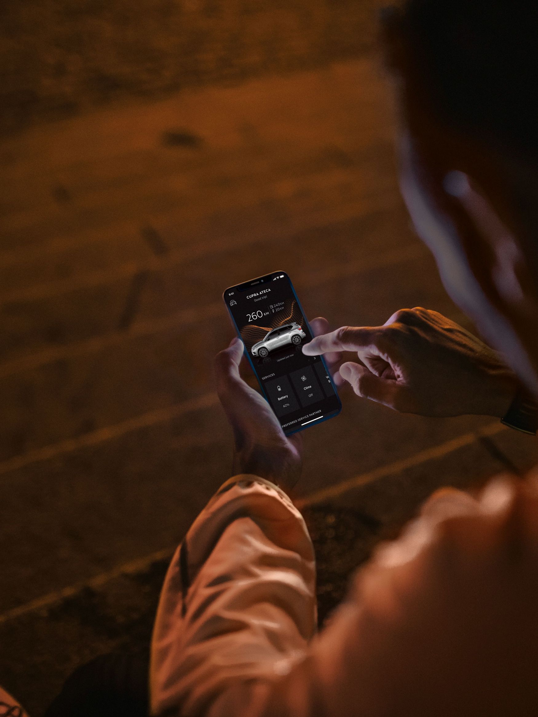 Eine Person sitzt nachts auf Treppenstufen und nutzt CUPRA Connect auf einem Smartphone.