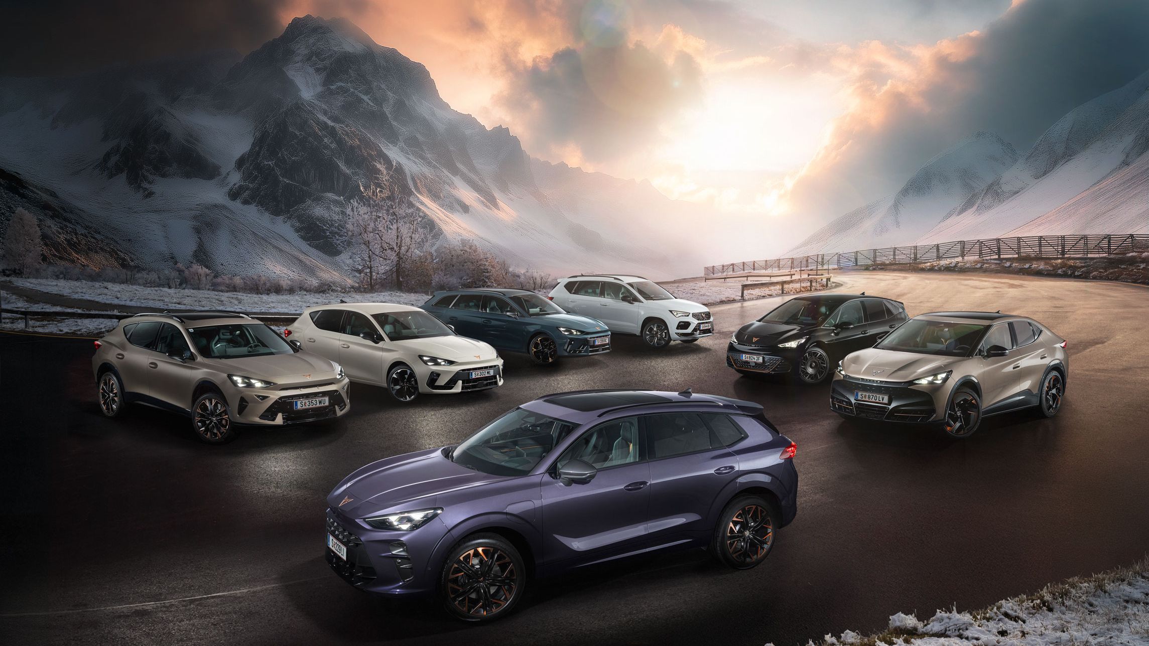 Eine Gruppe von CUPRA Fahrzeugen stehen auf einer verschneiten Straße vor einer malerischen Berglandschaft bei Sonnenuntergang. Es sind verschiedene Modelle in unterschiedlichen Farben. Im Hintergrund sind hohe, schneebedeckte Berge und dramatische Wolkenformationen zu sehen.