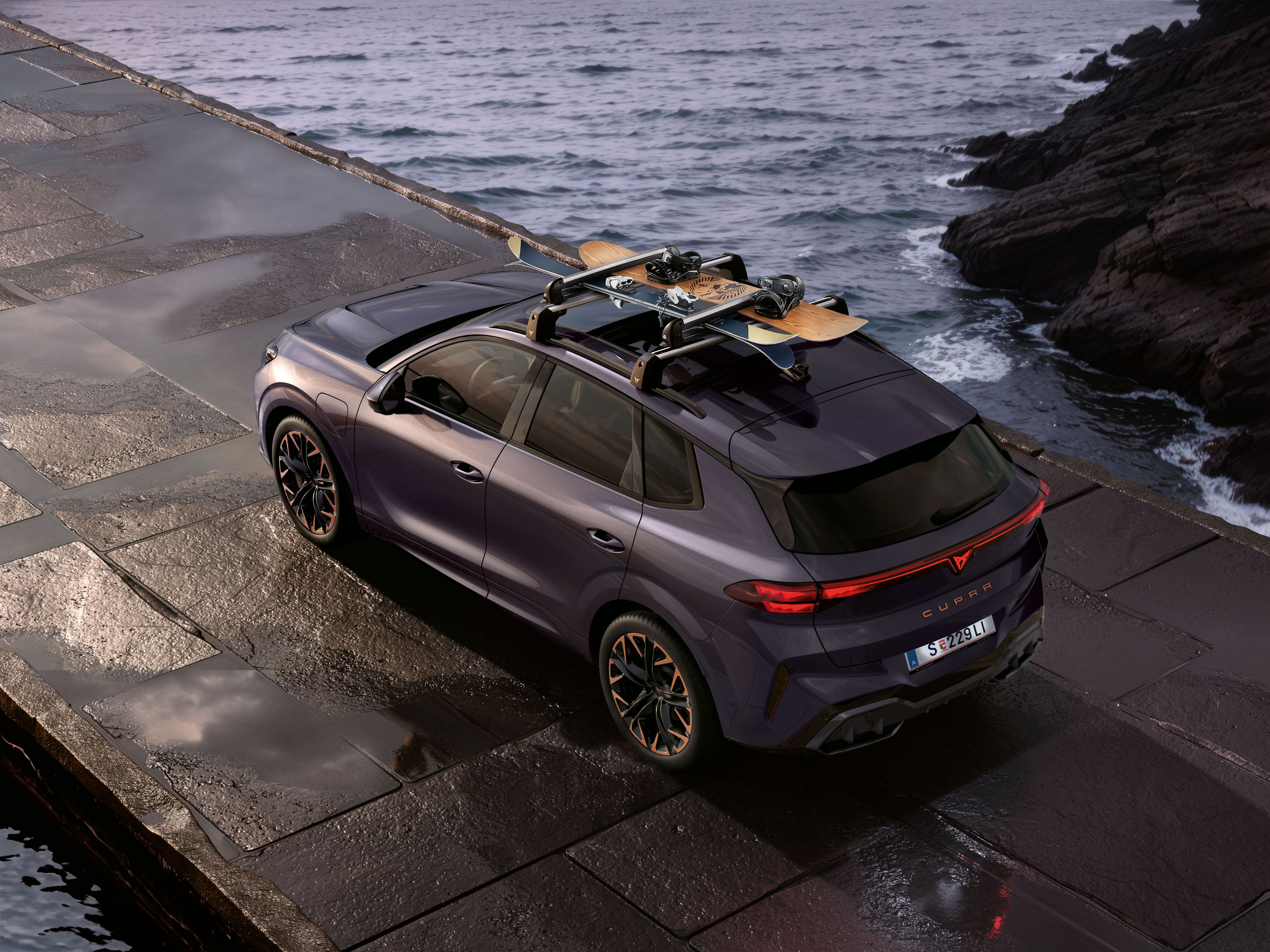 Ein CUPRA Terramar mit Dachträger parkt zwischen Felsen an der Meeresküste. Auf dem Dachträger ist ein Snowboard befestigt.