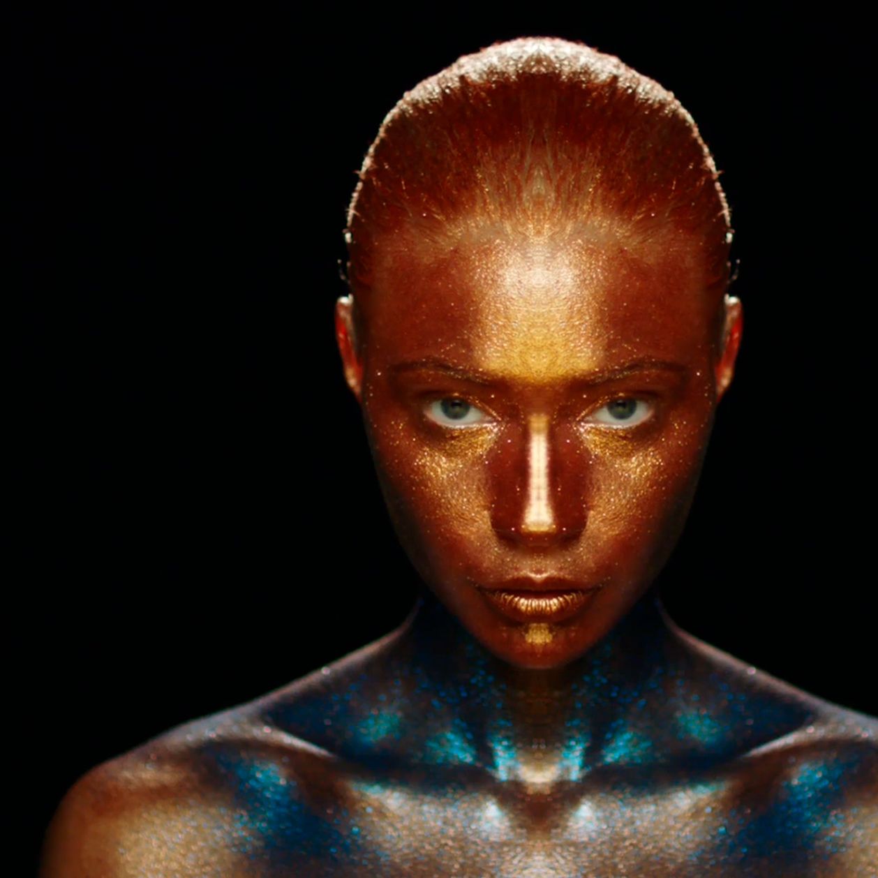 Eine Frau mit Ganzkörper Makeup in Gold und Türkis mit Glitter.