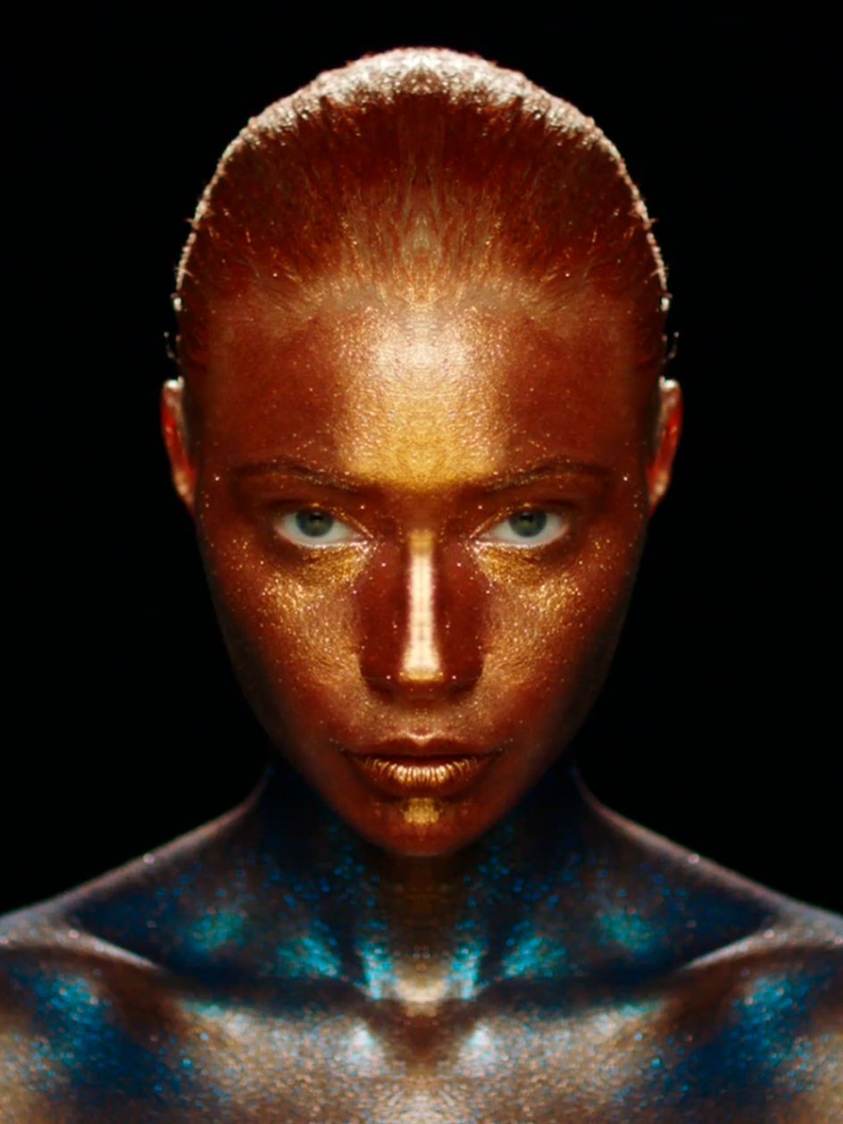 Eine Frau mit Ganzkörper Makeup in Gold und Türkis mit Glitter.