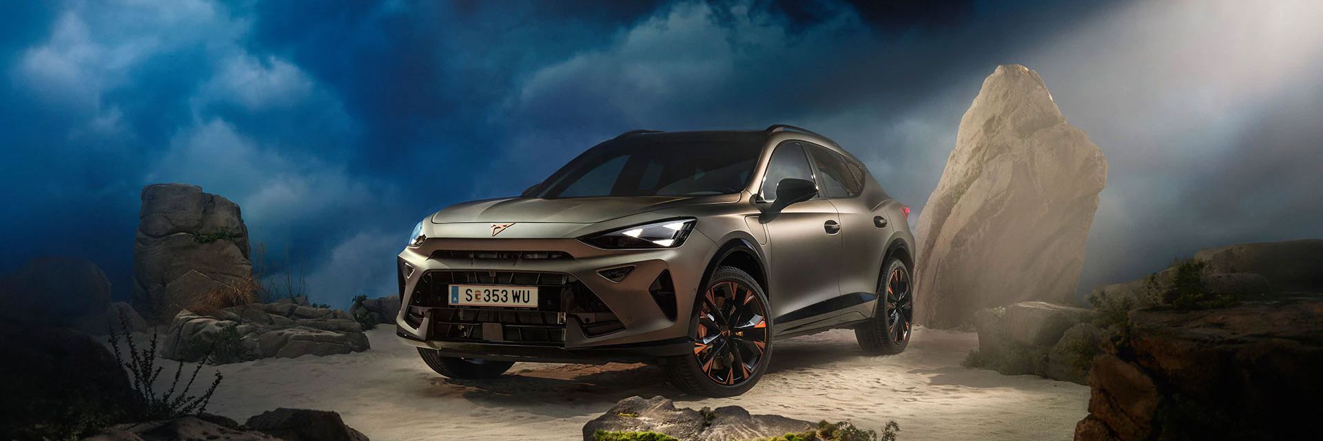 Ein CUPRA Formentor VZ in Bronze steht dramatisch beleuchtet in einer felsigen, nebeligen Landschaft. Eine Lichtstrahl beleuchtet das Fahrzeug und betont seine Konturen. Im Hintergrund sind Felsen und Pflanzen zu sehen.