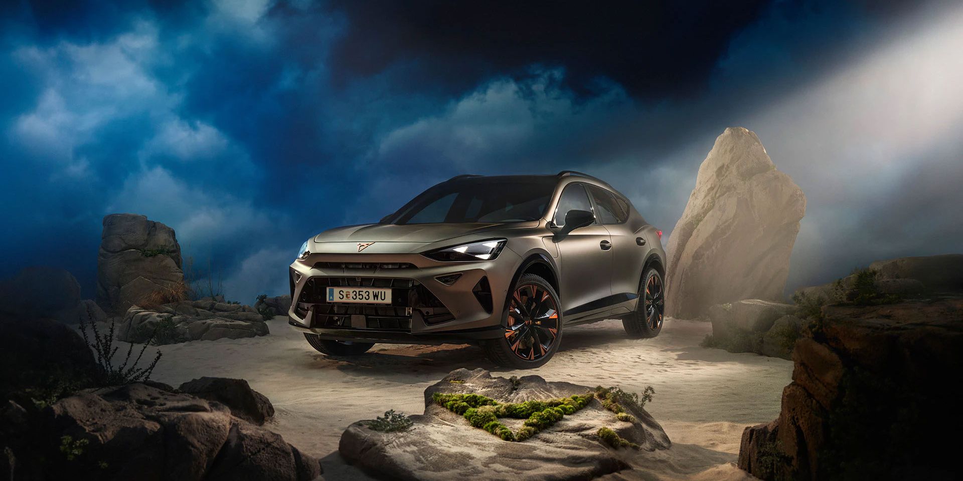 Ein CUPRA Formentor VZ in Bronze steht dramatisch beleuchtet in einer felsigen, nebeligen Landschaft. Eine Lichtstrahl beleuchtet das Fahrzeug und betont seine Konturen. Im Hintergrund sind Felsen und Pflanzen zu sehen.