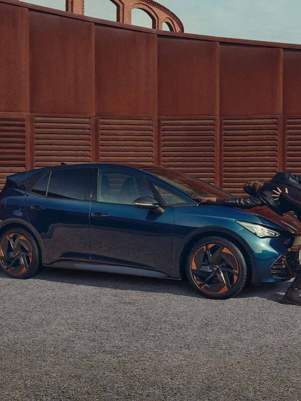 Ein blauer CUPRA Born steht auf einem Platz, Menschen performen neben dem Fahrzeug.