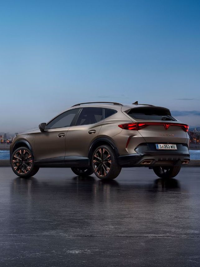 Ein CUPRA Formentor steht auf einer glatten Oberfläche vor einer Stadtlandschaft bei Sonnenaufgang. Im Hintergrund ist das Meer und hohe Gebäude zu sehen.