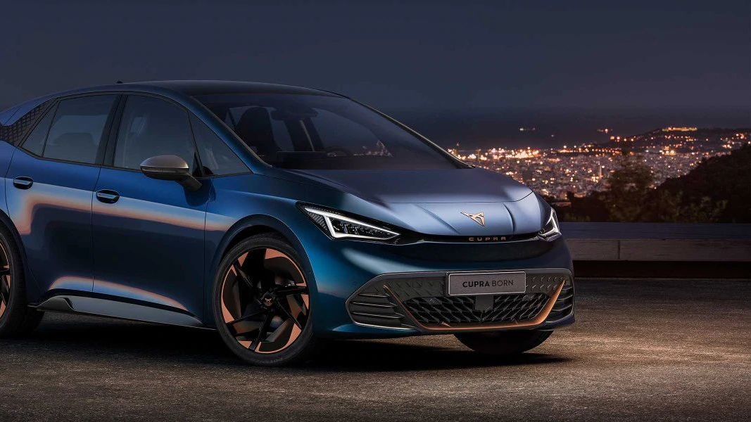 Schräge Frontansicht eines CUPRA Born bei Nacht vor der Silhouette einer Stadt.