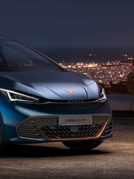 Schräge Frontansicht eines CUPRA Born bei Nacht vor der Silhouette einer Stadt.