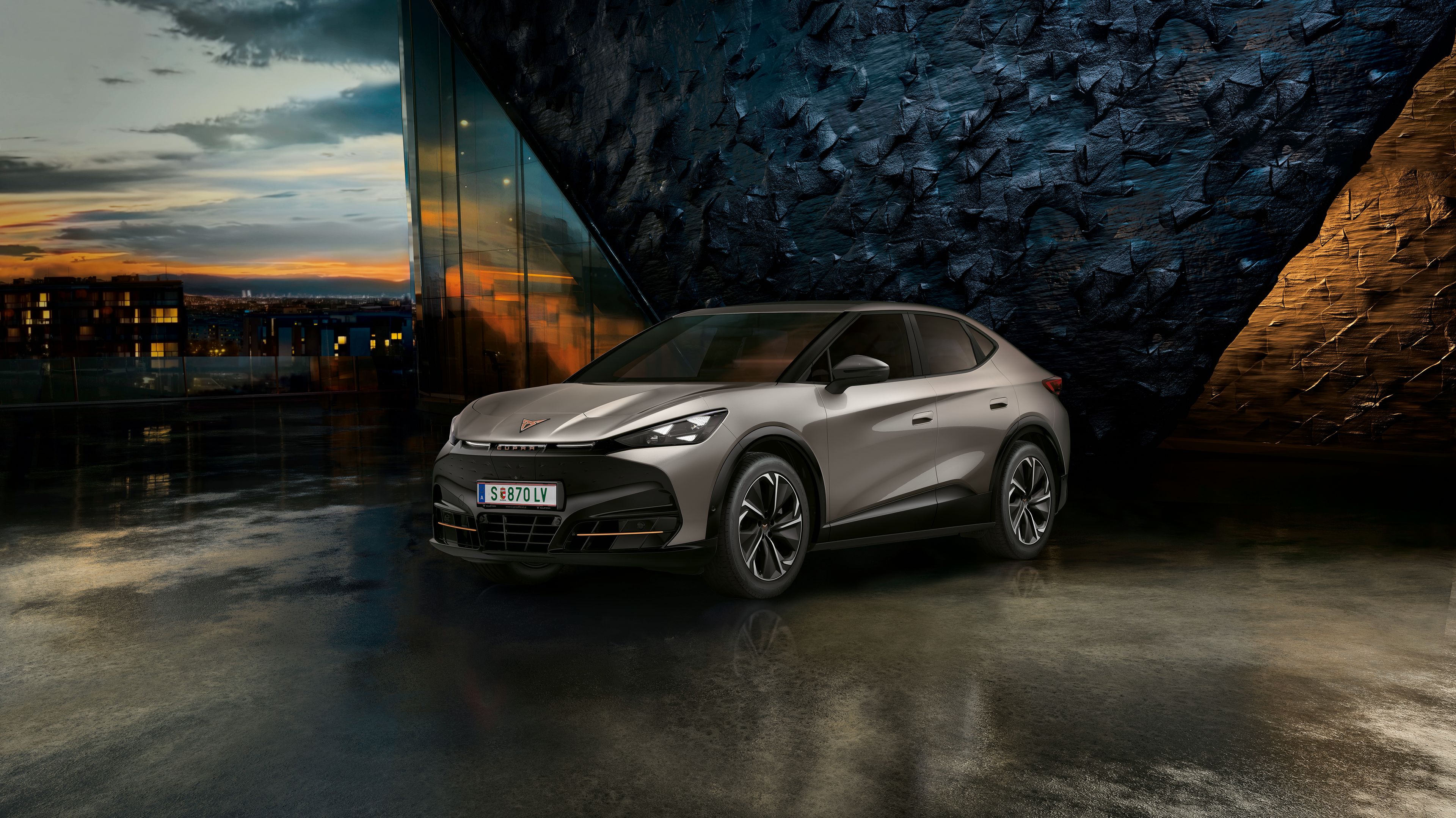 CUPRA Tavascan vor einer Steinwand bei Sonnenuntergang