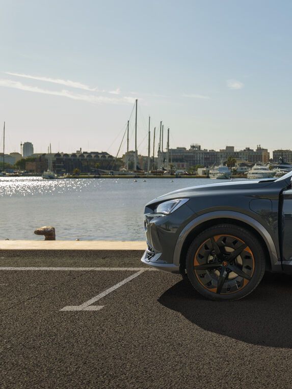 Eine Frau steht an der geöffneten Vordertüre eines grauen CUPRA Leon der am Kai eines Hafens parkt.