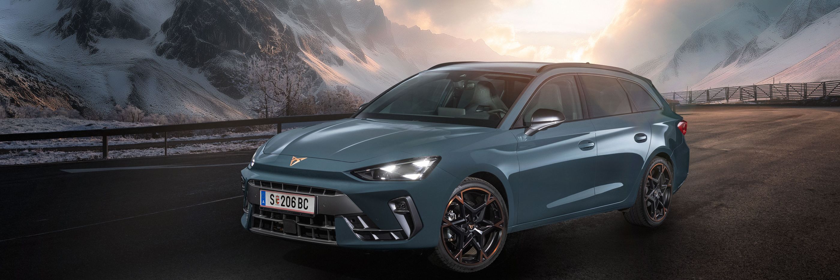 Ein CUPRA Leon Kombi parkt vor einer malerischen Berglandschaft bei Sonnenuntergang. Im Hintergrund sind verschneite Gipfel und dramatische Wolken zu sehen. Der Asphalt ist dunkel und feucht.