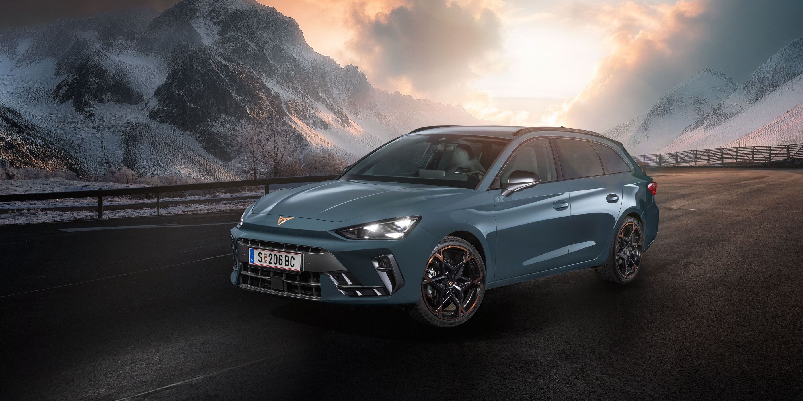 Ein CUPRA Leon Kombi parkt vor einer malerischen Berglandschaft bei Sonnenuntergang. Im Hintergrund sind verschneite Gipfel und dramatische Wolken zu sehen. Der Asphalt ist dunkel und feucht.