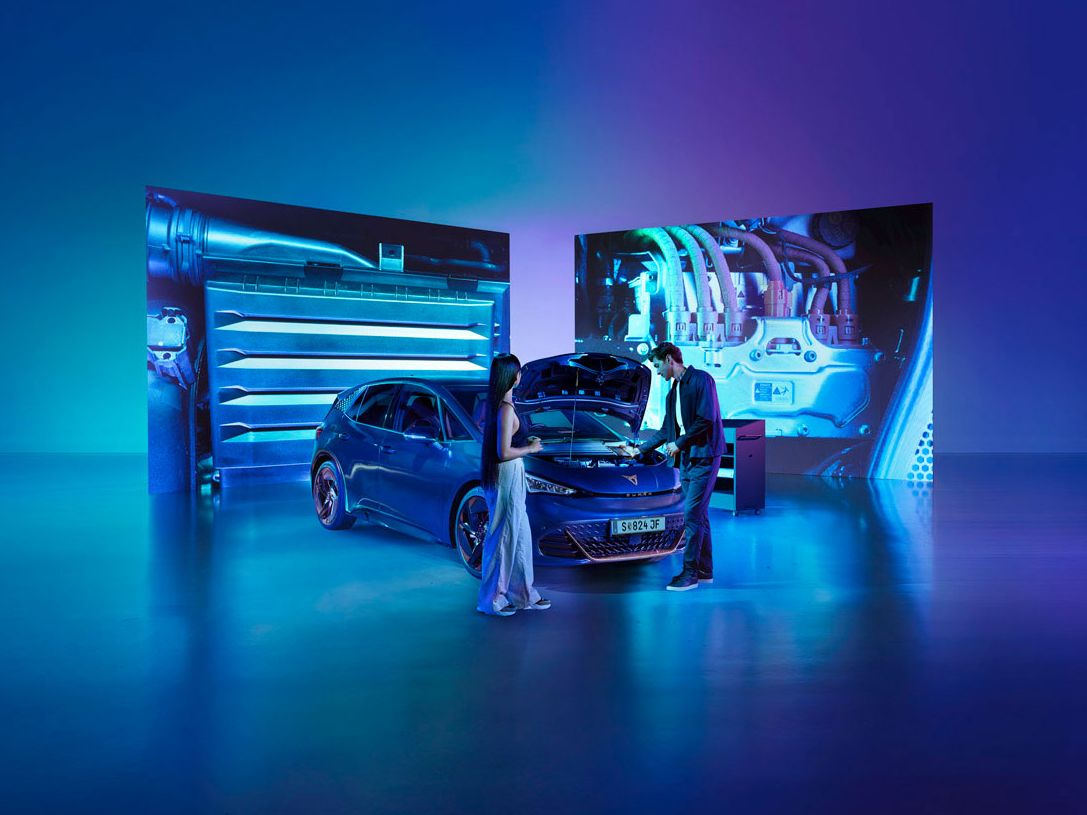 Eine Frau und ein Mann blicken bei geöffneter Kühlerhaube auf den Motor eines CUPRA Born