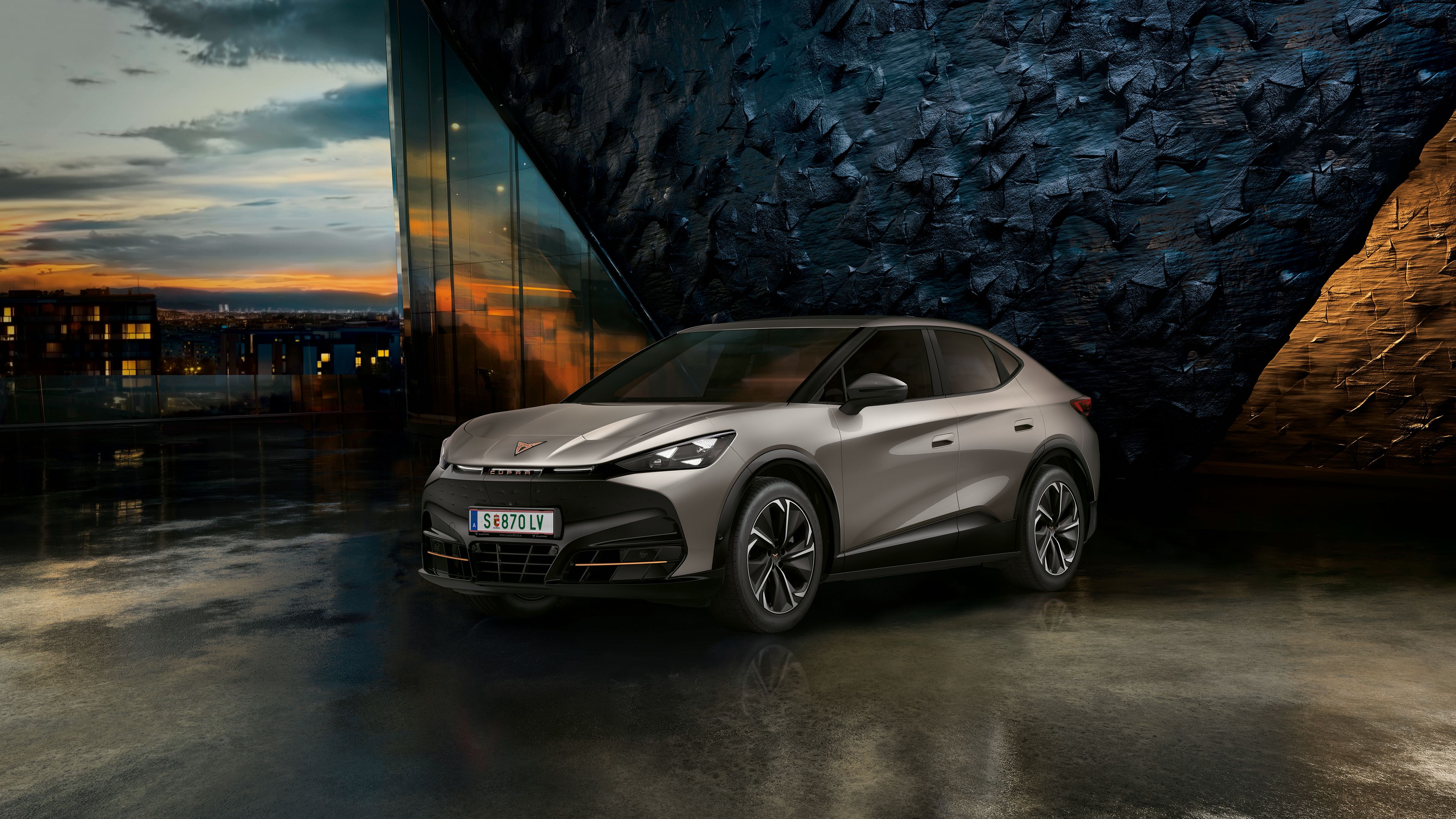 CUPRA Tavascan vor einer Steinwand bei Sonnenuntergang