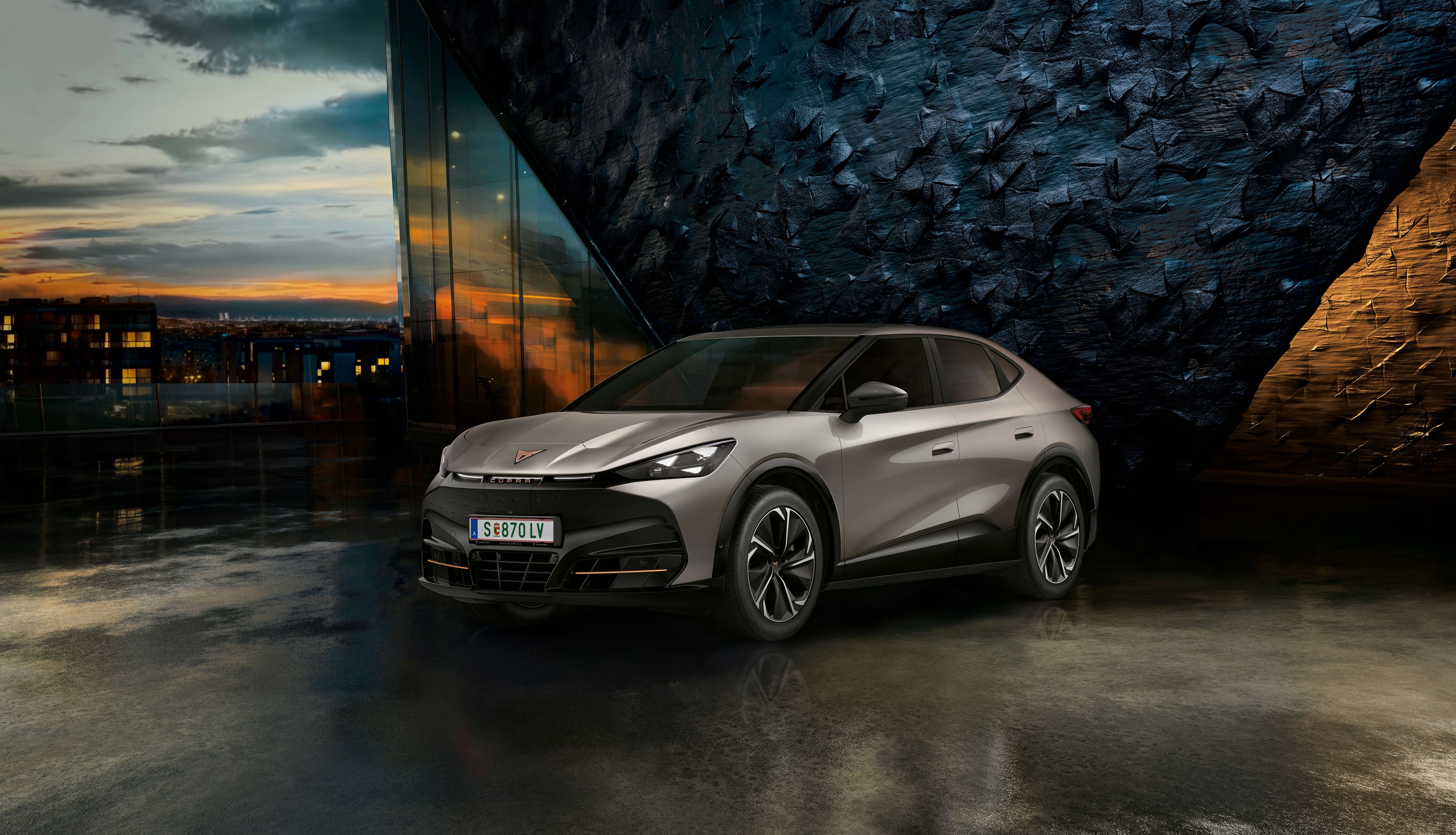 CUPRA Tavascan vor einer Steinwand bei Sonnenuntergang