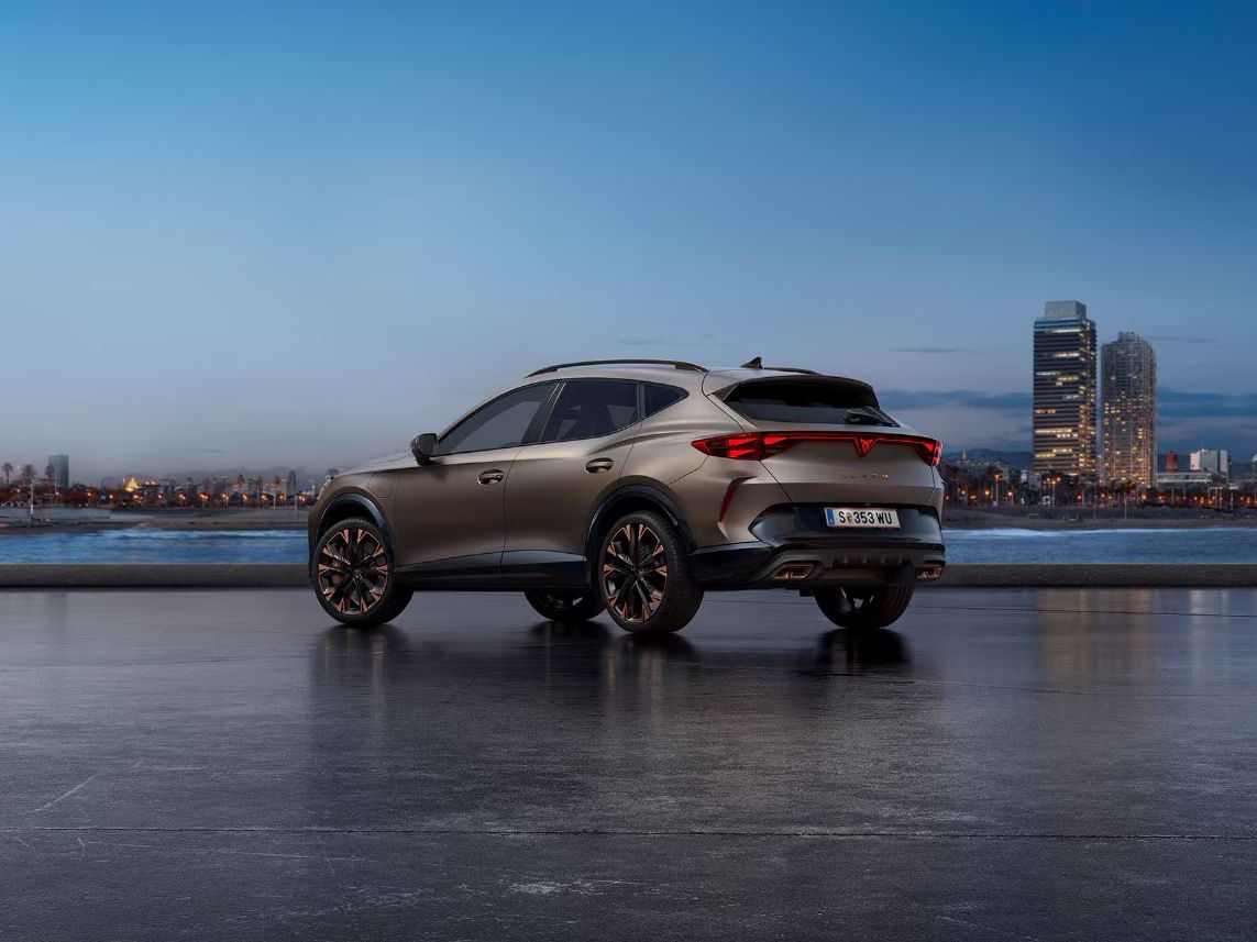 Ein CUPRA Formentor steht auf einer glatten Oberfläche vor einer Stadtlandschaft bei Sonnenaufgang. Im Hintergrund ist das Meer und hohe Gebäude zu sehen.