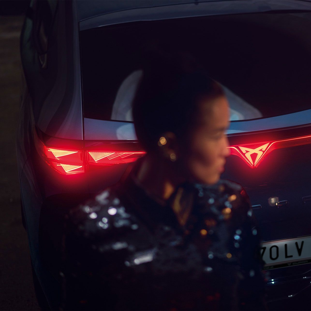 Detailaufnahme vom Heck eines CUPRA Tavascan mit durchgehender Heckbeleuchtung, eine Frau steht neben dem Fahrzeug.