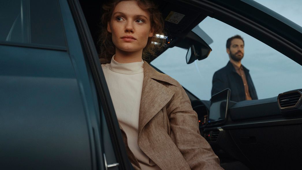 Eine Frau sitzt bei geöffneter Fahrzeugtür auf dem Beifahrersitz eines CUPRA Formentor. Im Hintergrund ist ein Mann zu sehen.
