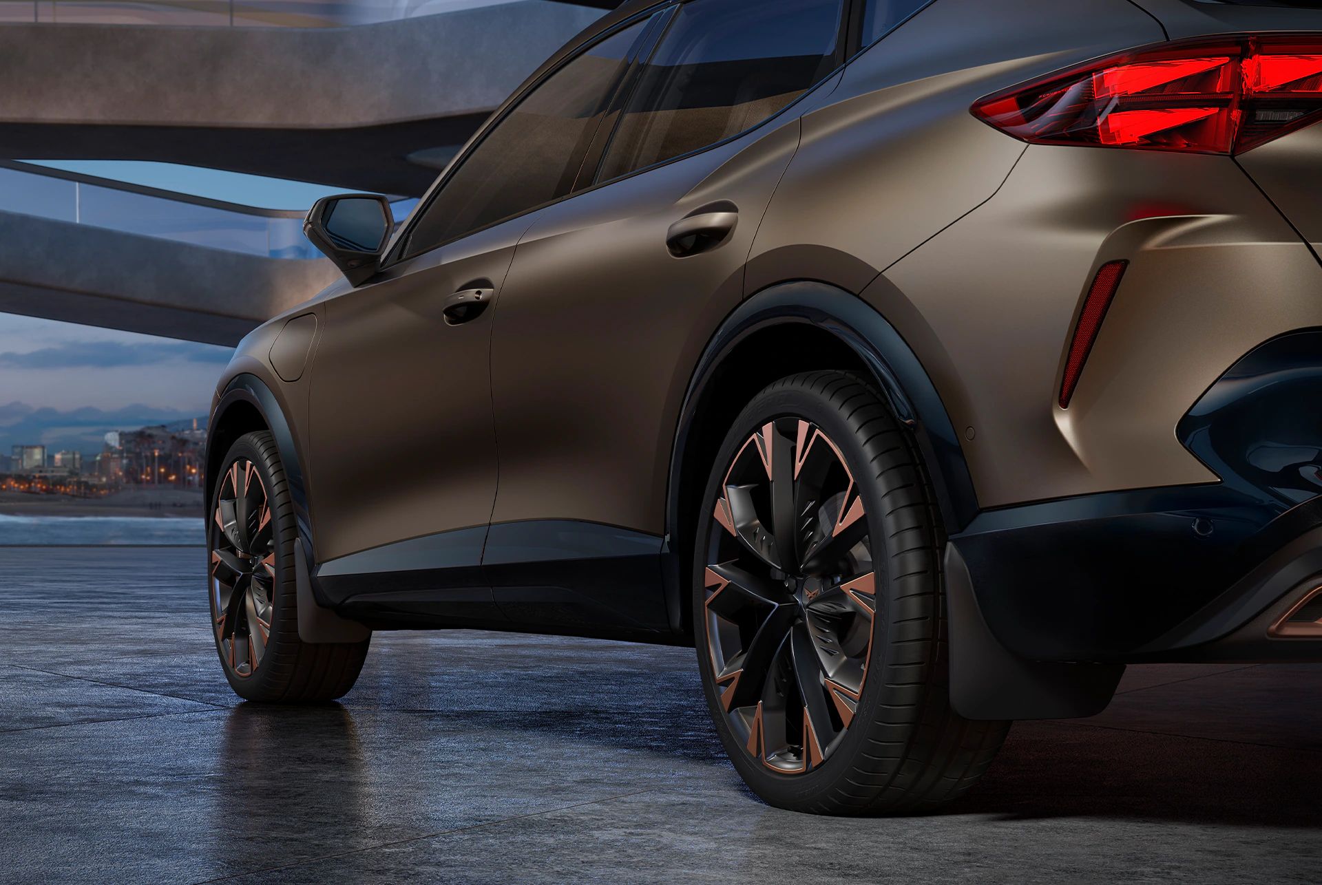 Ein CUPRA Formentor in einer Garage, mit Detailansicht auf die Hinterräder und Schmutzfänger. Das Fahrzeug ist in Bronze lackiert. Im Hintergrund sind architektonische Strukturen und eine Stadtlandschaft bei Dämmerung zu sehen.