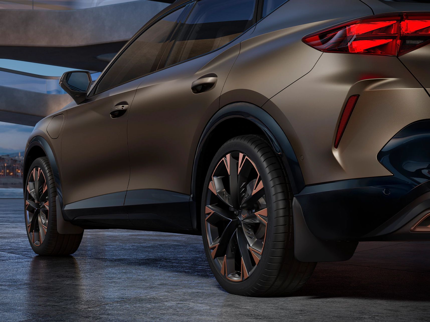 Ein CUPRA Formentor in einer Garage, mit Detailansicht auf die Hinterräder und Schmutzfänger. Das Fahrzeug ist in Bronze lackiert. Im Hintergrund sind architektonische Strukturen und eine Stadtlandschaft bei Dämmerung zu sehen.
