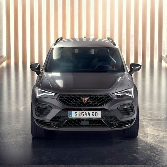 Eine Frontansicht des CUPRA Ateca, eines grauen SUVs, in einer modernen, beleuchteten Umgebung. Das Bild hebt die markante Frontpartie, die LED-Scheinwerfer und das elegante Design des Fahrzeugs hervor.