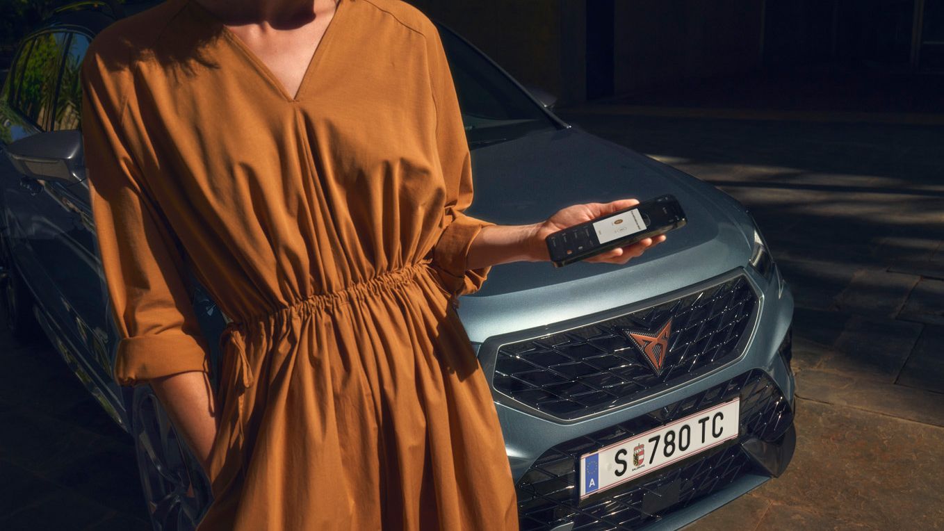 Eine Frau neben einem CUPRA Formentor blickt auf ihr Smartphone.