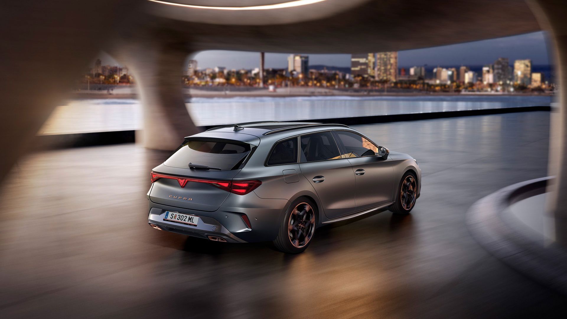 Schräge hintere Seitenansicht eines grauen CUPRA Leon Sportstourer auf der Fahrt durch ein modernes Parkhaus.