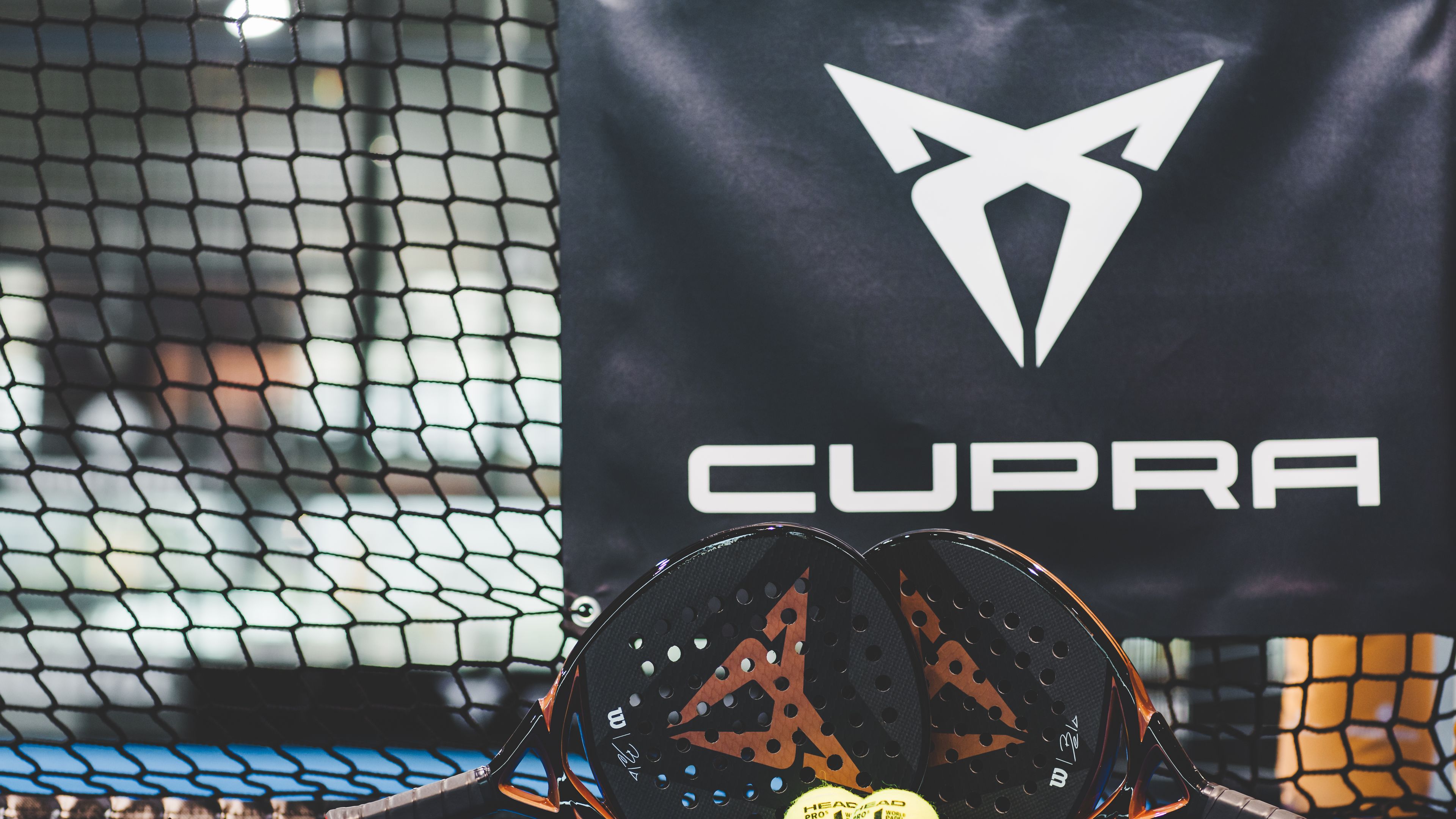 Zwei CUPRA Padels und zwei Bälle vor einem CUPRA Logo.