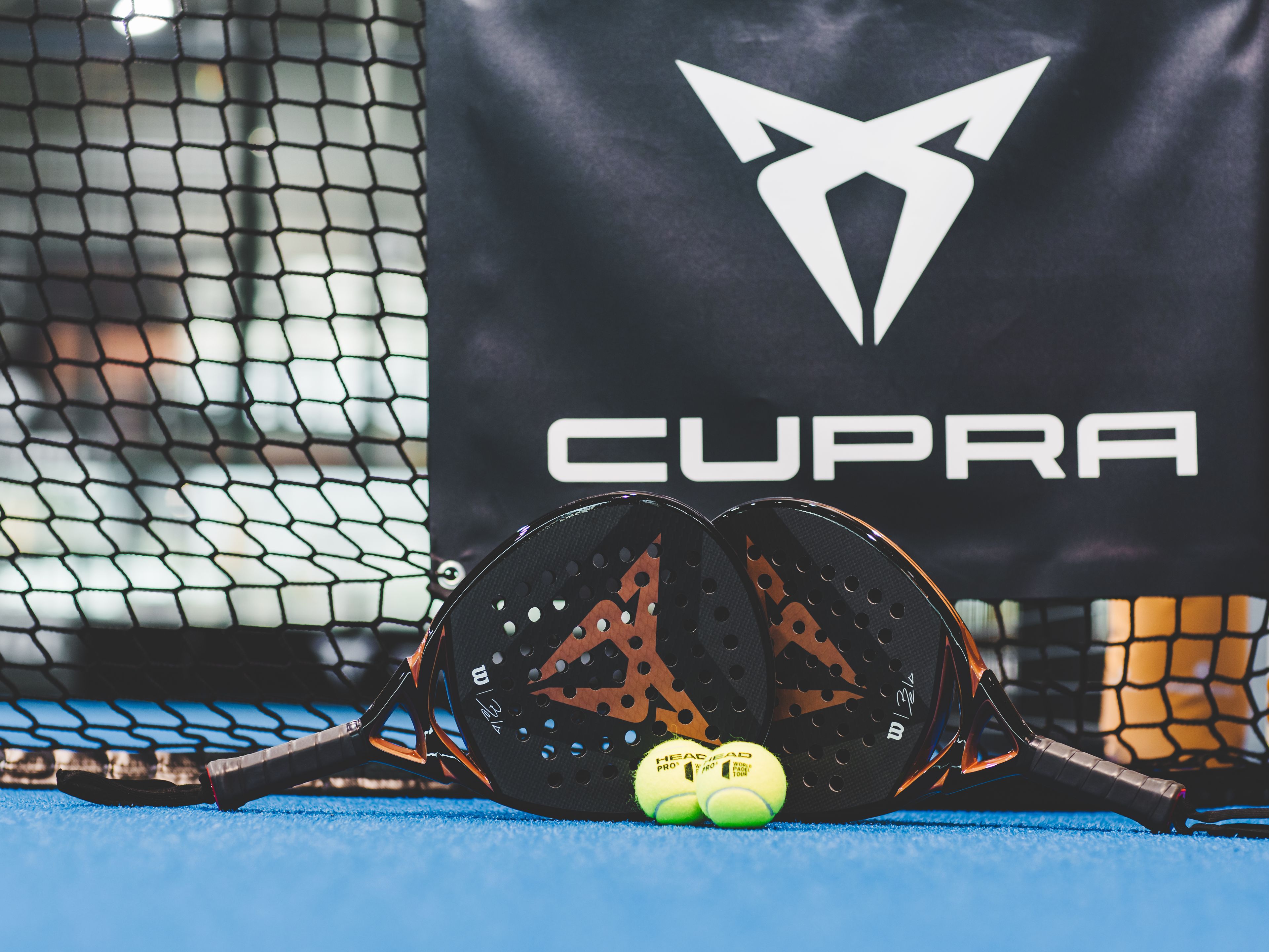 Zwei CUPRA Padels und zwei Bälle vor einem CUPRA Logo.