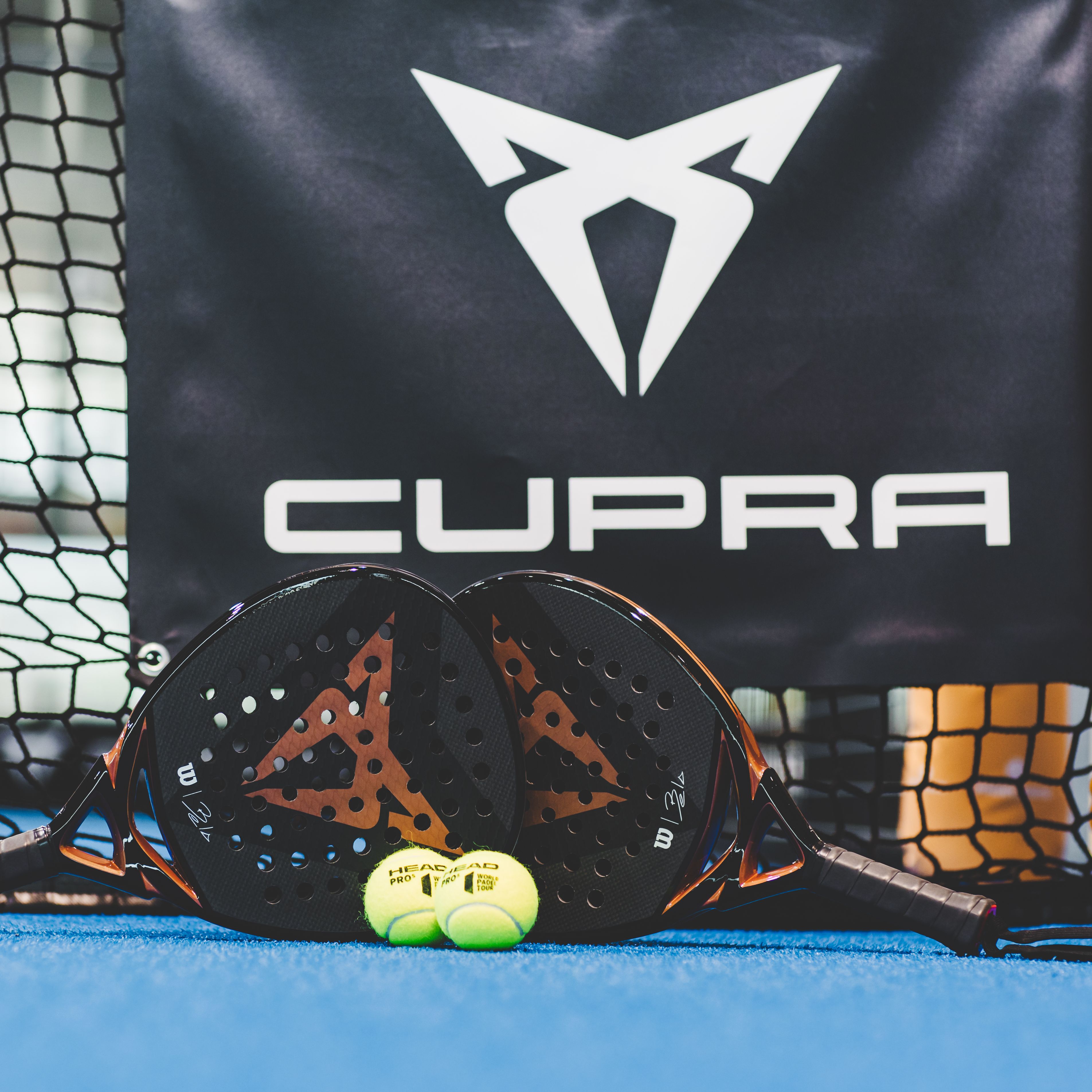 Zwei CUPRA Padels und zwei Bälle vor einem CUPRA Logo.