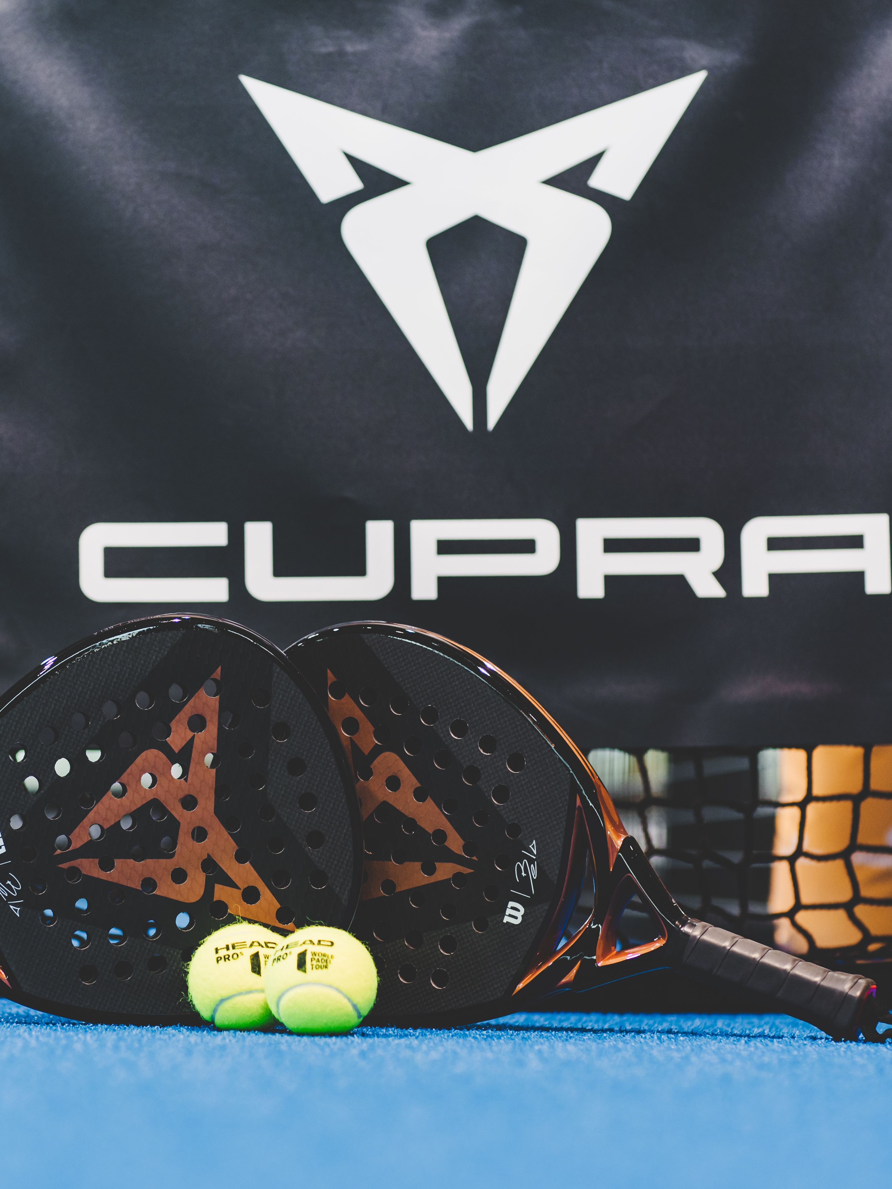 Zwei CUPRA Padels und zwei Bälle vor einem CUPRA Logo.