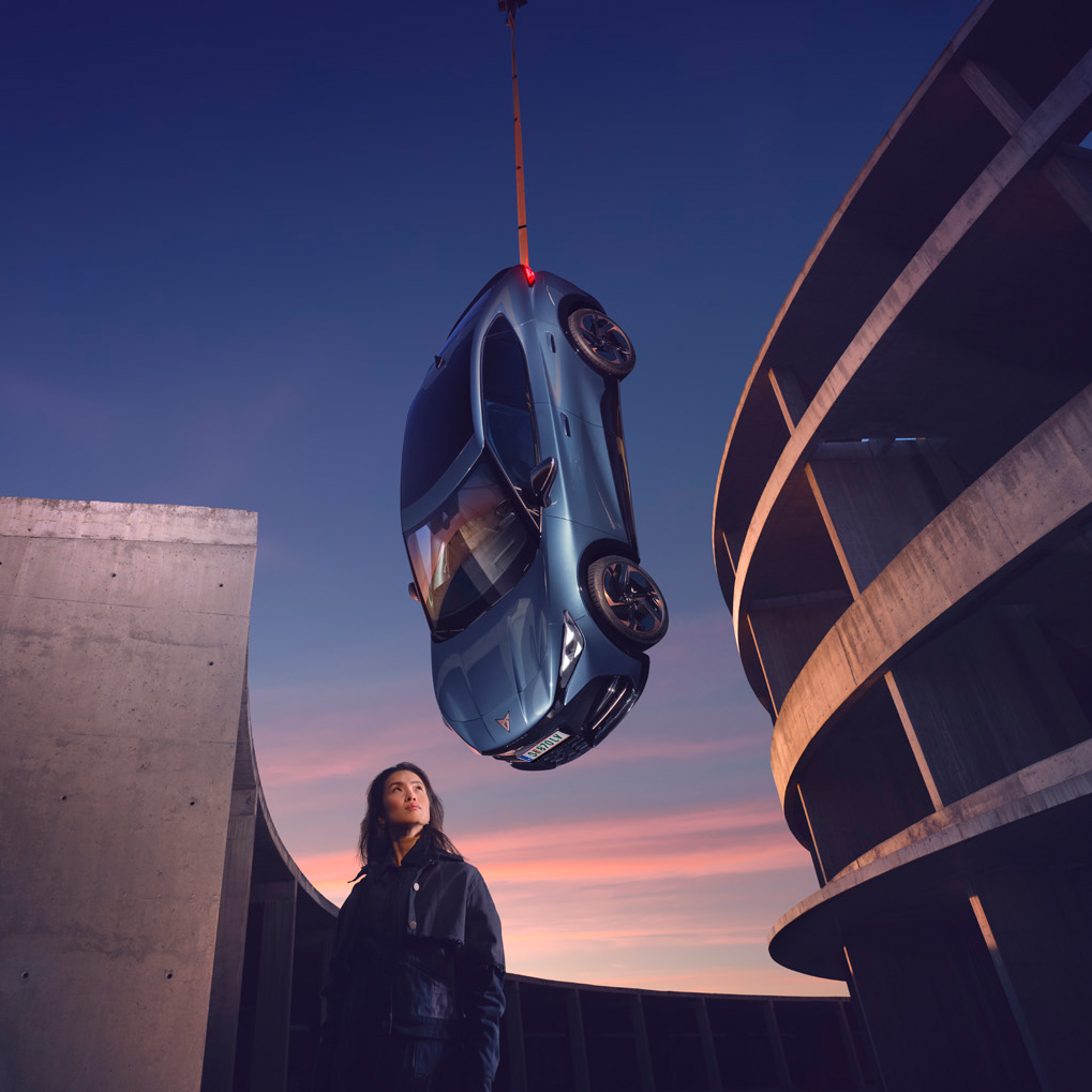 CUPRA Tavascan hängt an einem Seil vom Himmel. Eine Frau steht darunter.
