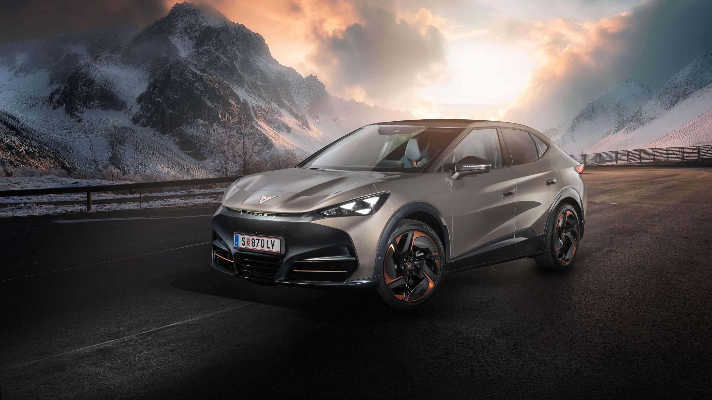 Ein CUPRA Tavascan steht auf einer Straße in einer bergigen Landschaft. Der Himmel zeigt dramatische Wolkenformationen bei Sonnenuntergang. Im Hintergrund sind schneebedeckte Gipfel zu sehen.