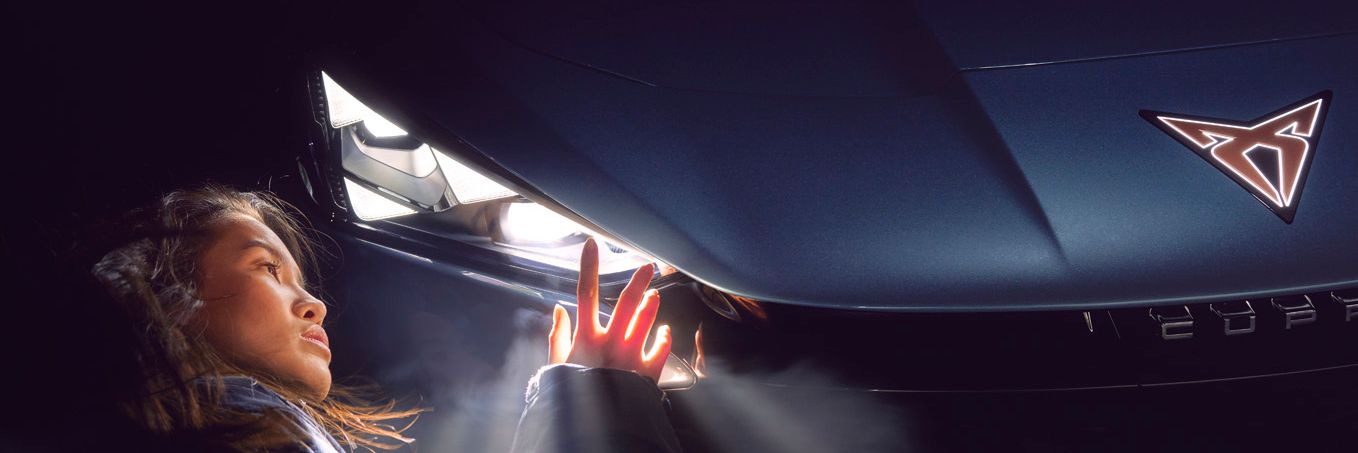 Eine Frau berührt den leuchtenden Scheinwerfer eines CUPRA Tavascan.