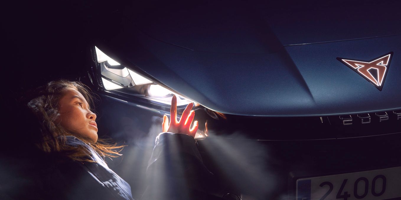 Eine Frau berührt den leuchtenden Scheinwerfer eines CUPRA Tavascan.