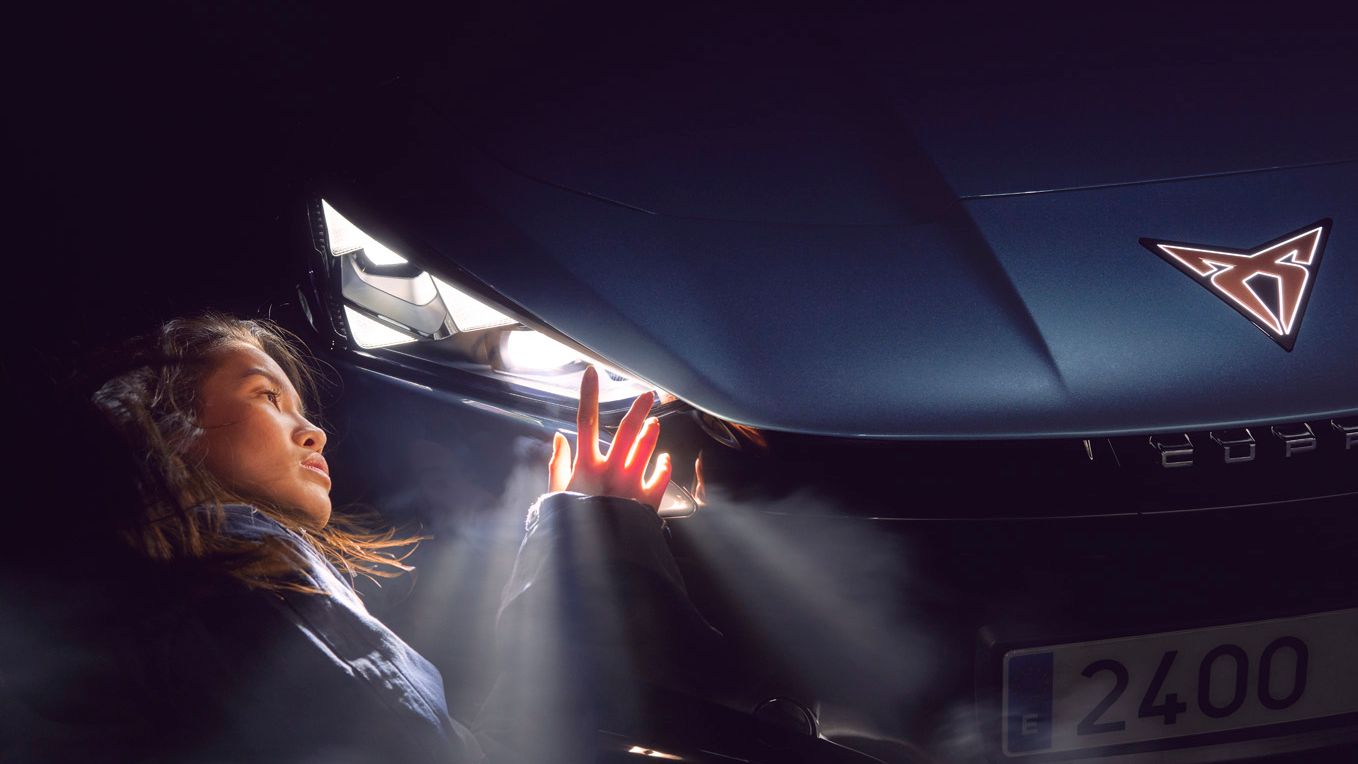 Eine Frau berührt den leuchtenden Scheinwerfer eines CUPRA Tavascan.