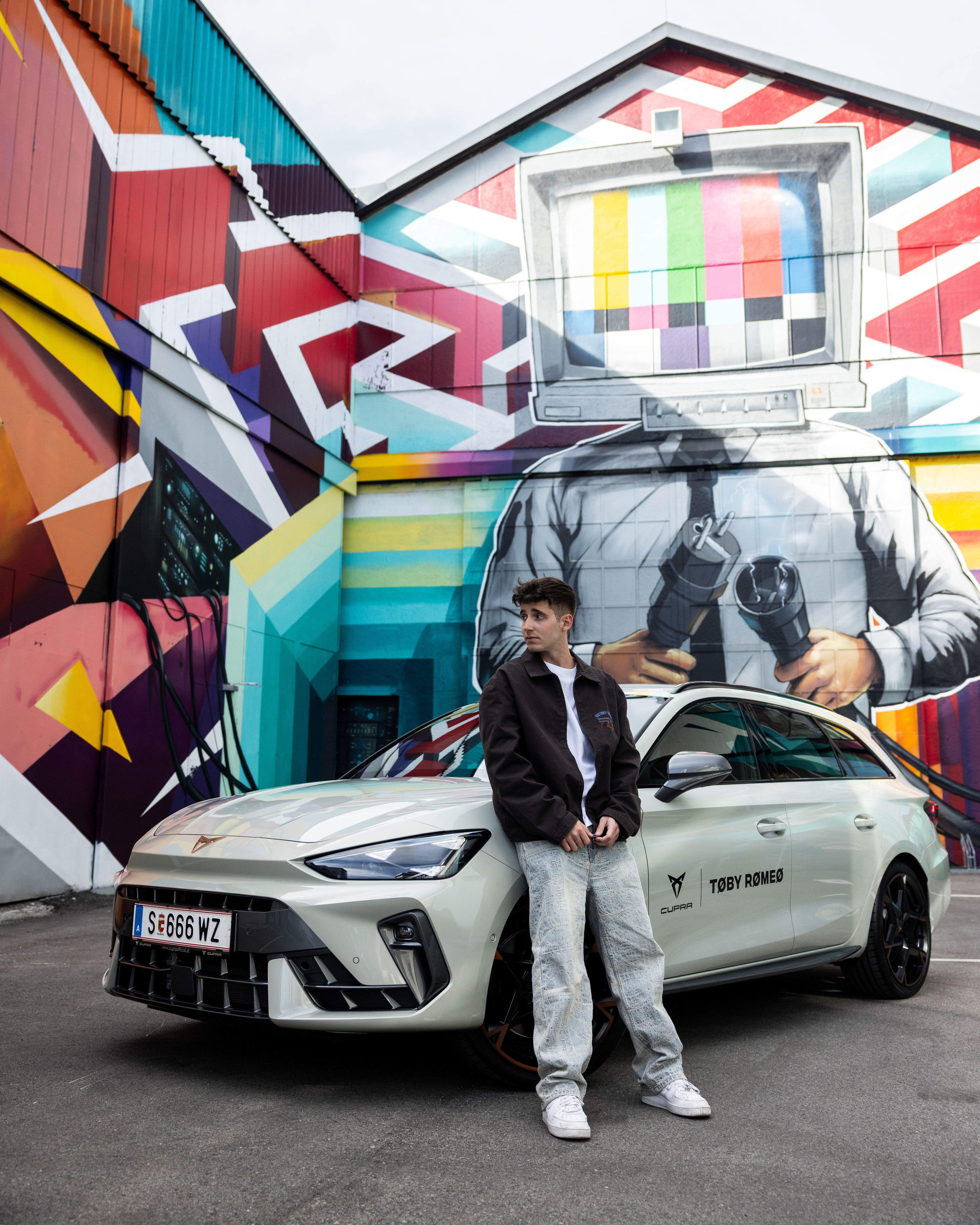 Toby Romeo lehnt an einem weißen CUPRA Formentor. Im Hintergrund Graffitis an einer Wand.