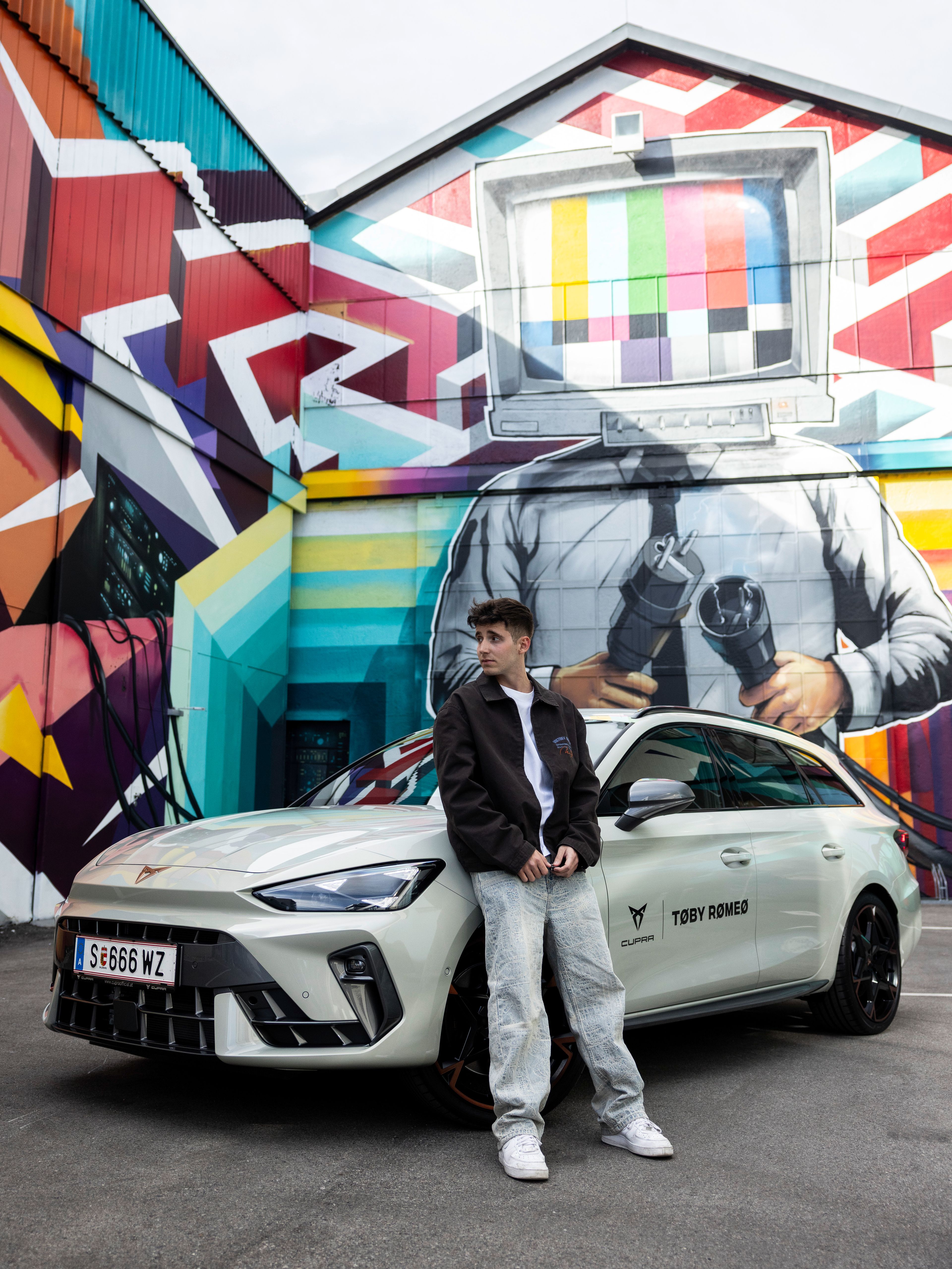 Toby Romeo lehnt an einem weißen CUPRA Formentor. Im Hintergrund Graffitis an einer Wand.