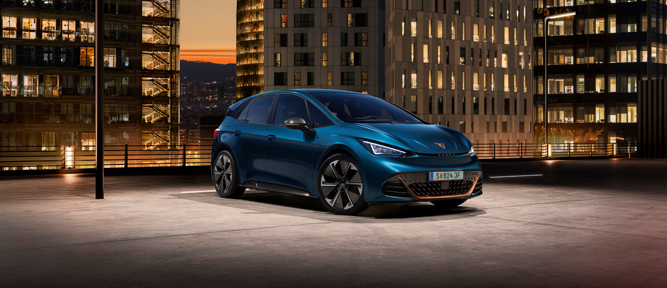 Ein blauer CUPRA Born auf dem Dach eines Parkhauses. Im Hintergrund beleuchtete Gebäude bei Nacht.
