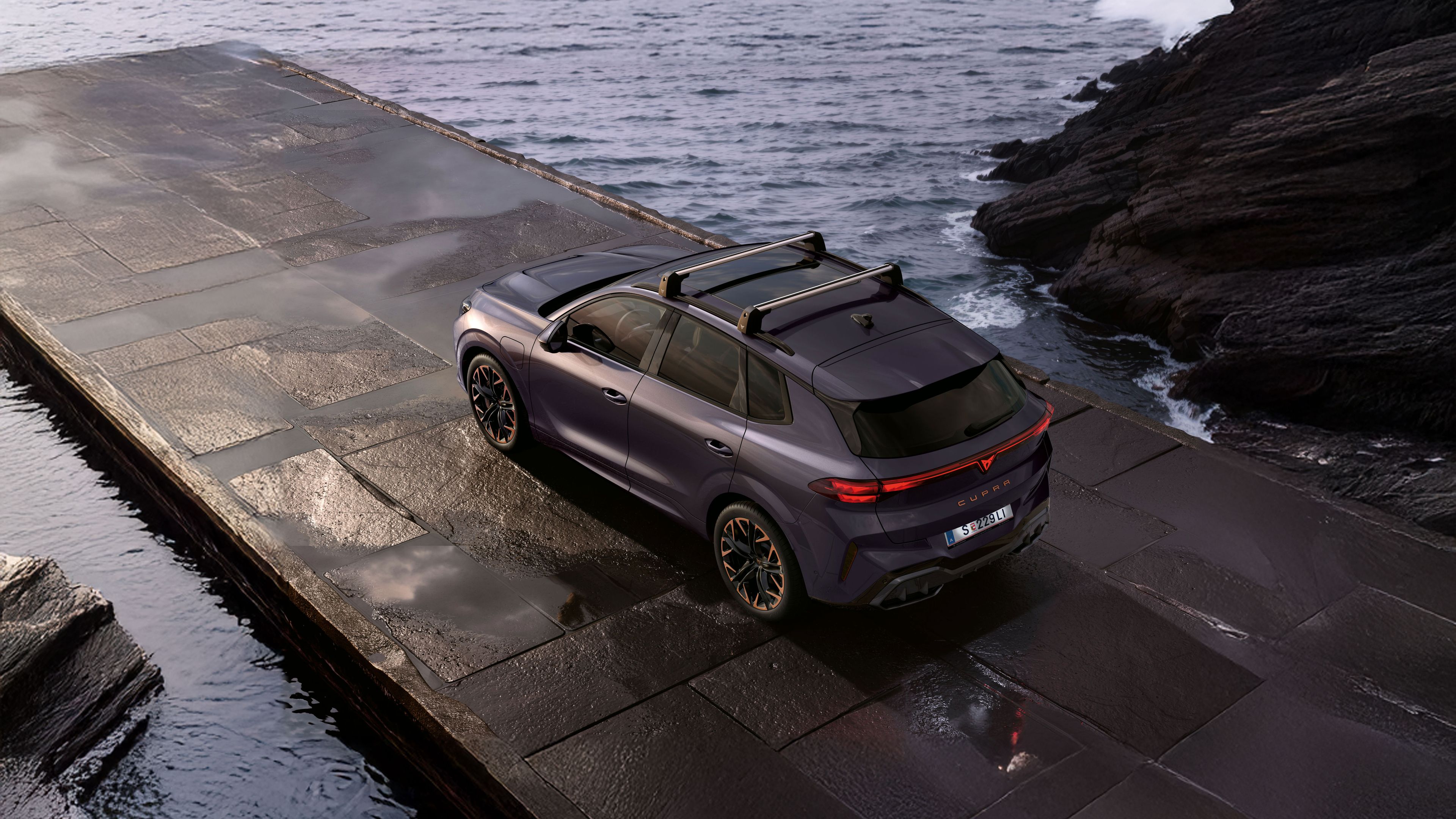 Seitlicher Blick von oben auf einen CUPRA Terramar. Das Fahrzeug parkt zwischen Felsen an einer Küste.