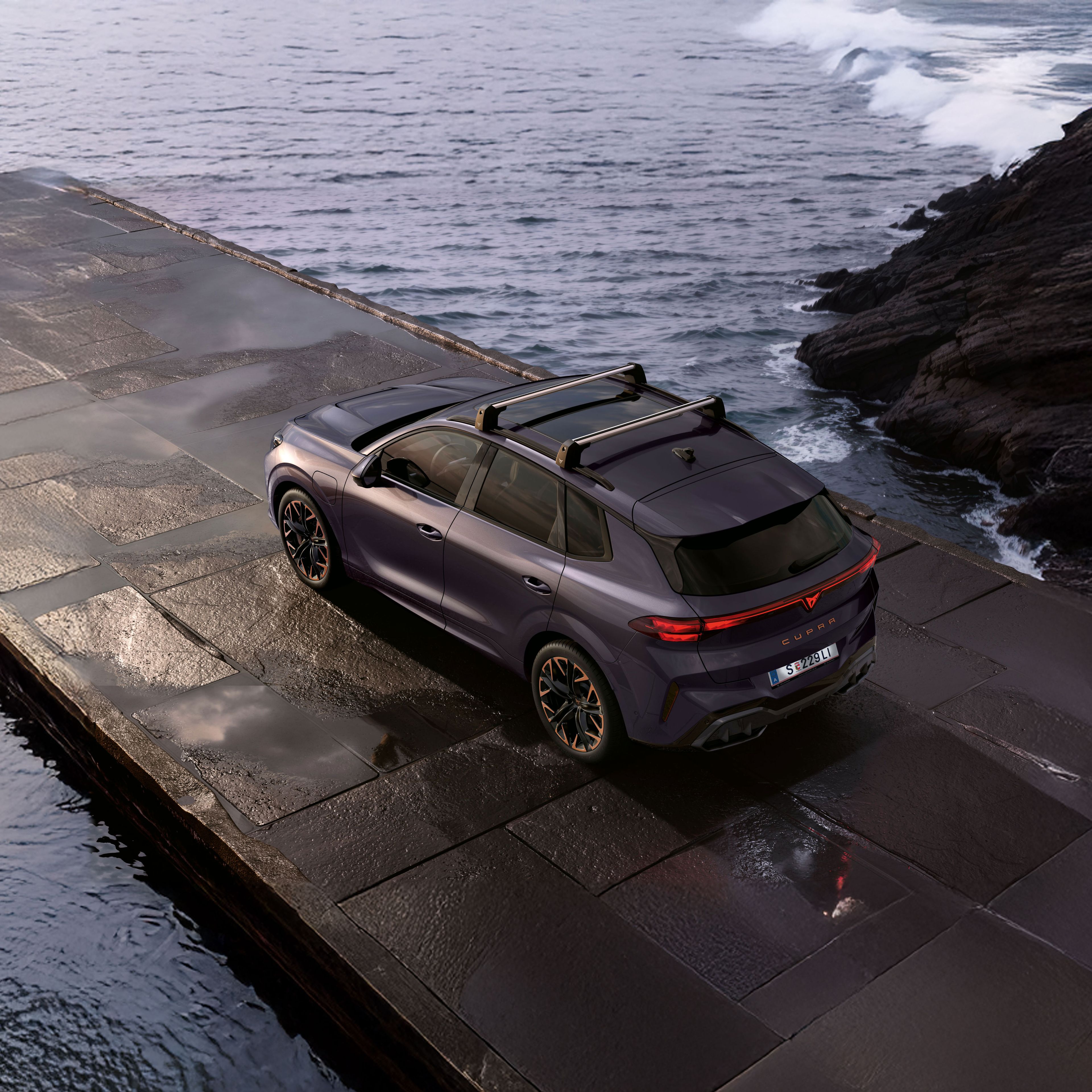 Seitlicher Blick von oben auf einen CUPRA Terramar. Das Fahrzeug parkt zwischen Felsen an einer Küste.