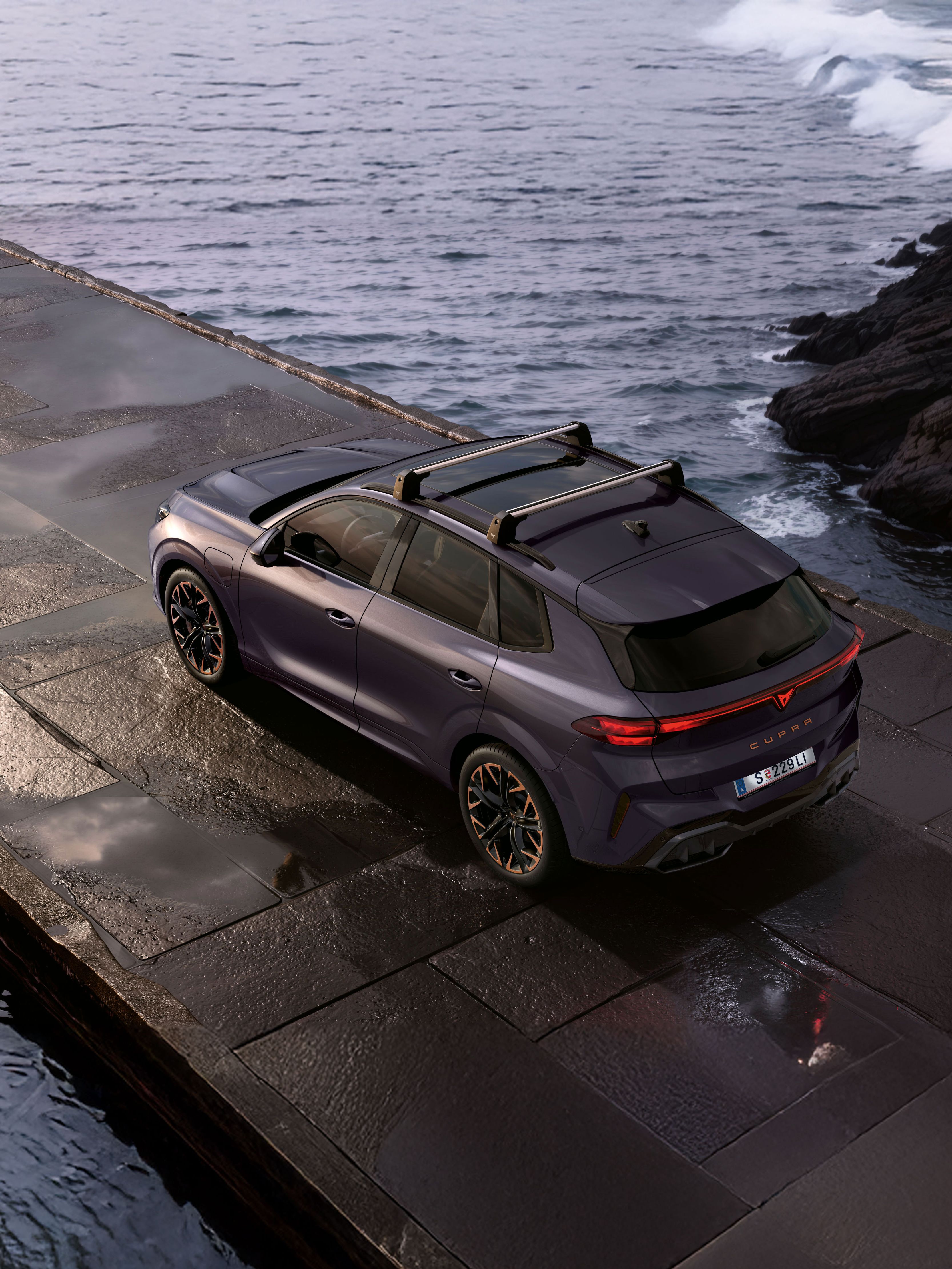 Seitlicher Blick von oben auf einen CUPRA Terramar. Das Fahrzeug parkt zwischen Felsen an einer Küste.