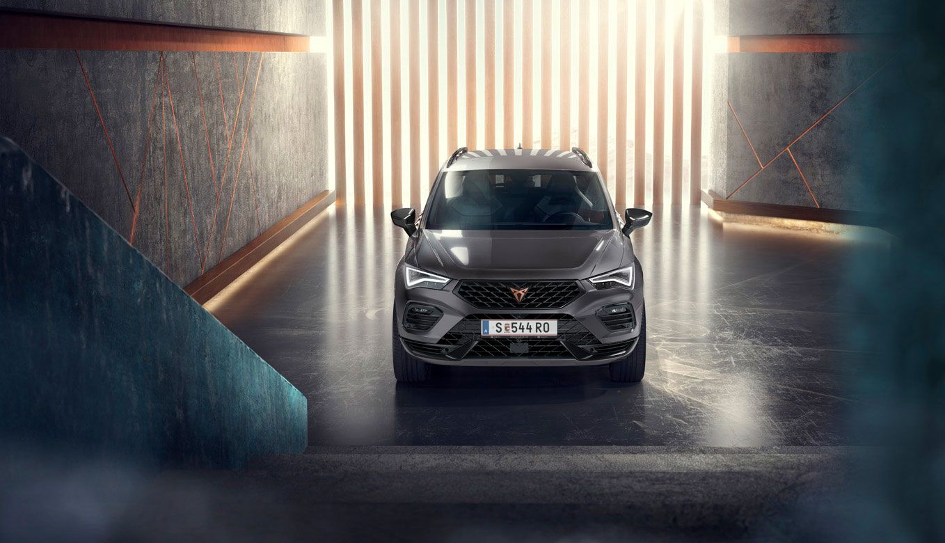 Eine Frontansicht des CUPRA Ateca, eines grauen SUVs, in einer modernen, beleuchteten Umgebung. Das Bild hebt die markante Frontpartie, die LED-Scheinwerfer und das elegante Design des Fahrzeugs hervor.