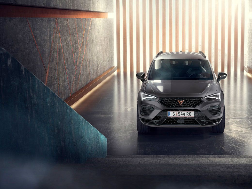 Eine Frontansicht des CUPRA Ateca, eines grauen SUVs, in einer modernen, beleuchteten Umgebung. Das Bild hebt die markante Frontpartie, die LED-Scheinwerfer und das elegante Design des Fahrzeugs hervor.